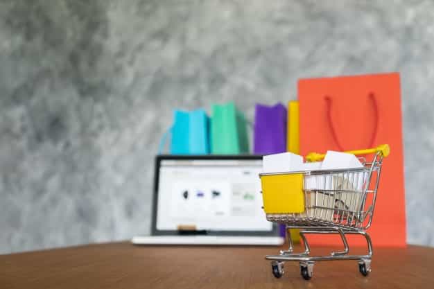A shopping cart on a table with a laptop and paper bags.